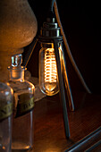 Elektrisches Licht mit Glühfaden und alten Medizinflaschen in einem Haus in Sussex, England