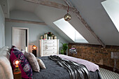 Double bed with dormer windows and exposed brick wall in attic conversion of Sussex farmhouse  UK