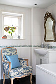 Light blue cushion on toile de jouy chair below square window in bathroom of UK home