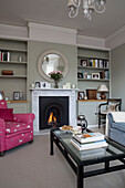 Rosa gepolsterter Sessel am beleuchteten Kamin im Wohnzimmer von Shoreham by Sea home West Susses England UK