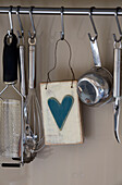 Kitchenware and heart ornament hang from utensil rail in Suffolk farmhouse kitchen,  England,  UK