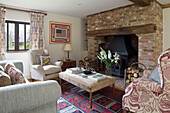 Exposed brick fireplace with armchairs and ottoman footstool in Suffolk farmhouse,  England,  UK