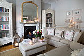 Lit candles with bookcases in living room with cream sofas in Hertfordshire home,  England,  UK