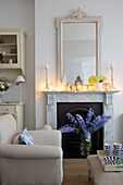 Lit candles on marble fireplace with cream armchair in Hertfordshire living room,  England,  UK