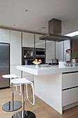 Stainless steel extractor above kitchen island with barstools in Hertfordshire home,  England,  UK