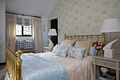 Brass bed with light blue patterned wallpaper and gingham cushions on window seat in Sussex cottage   England   UK