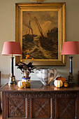 Pair of lamps on carved sideboard with gilt-framed artwork in hallway of London home,  England,  UK