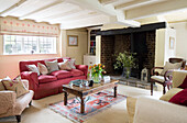 Rotes Sofa und hölzerner Couchtisch mit freiliegendem Backsteinkamin im Wohnzimmer eines Bauernhauses in Großbritannien