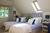 Twin beds with patterned headboard below velux window in UK farmhouse