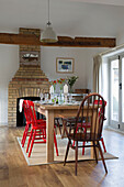 Wooden dining table with painted chairs and exposed brick chimney breast in London home,  England,  UK