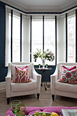 Pair of armchairs with pink floral cushions in bay window of London home,  England,  UK