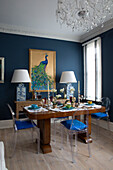 Polished wooden table in blue dining room with gilded peacock artwork and lamps in London home,  England,  UK