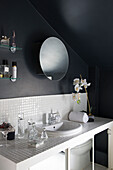 Weiß gefliester Waschbeckenrand in schwarzem Badezimmer mit rundem Spiegel, London, England, UK