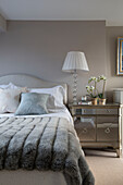 White lamp and orchid on mirrored cabinet with grey blanket on bed in London home,  England,  UK