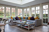 Purple and yellow cushions on sofa with coffee table in conservatory of Surrey home,  England,  UK