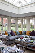 Purple and yellow cushions on sofa under skylight in conservatory of Surrey home,  England,  UK