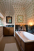 Kerzen auf der holzgetäfelten Badewanne in einem voll tapezierten Zimmer im Haus in Lymington, Hampshire, Großbritannien