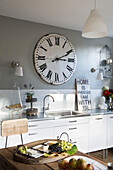 Large vintage clock above sink in Berkshire kitchen with cheeseboard,  England,  UK