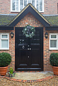 Christmas wreath above black front door of brick Chobham home   Surrey   England   UK