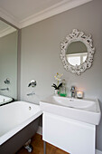 Decorative mirror above washbasin with lit candle next to freestanding bath in Chobham home   Surrey   England   UK