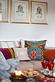 Patterned cushion on sofa below gilt-framed prints with lit candles and mince pies in Surrey living room   England   UK