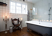 Beleuchtete Kerzen und Holzstuhl mit grauer freistehender Badewanne Surrey home England UK