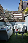 Armchair and sofa with table on astroturf in fenced backyard of London townhouse   England   UK