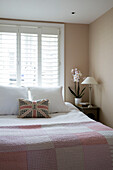 Union Jack cushion on pink gingham quilted double bed at shuttered window in London townhouse   England   UK