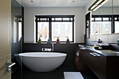 Freestanding bath at window of bathroom with double basins and mirrored cabinets in London home,  England,  UK