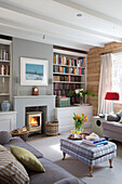 Light grey sofas in wood panelled living room with lit fire in Surrey home, England, UK