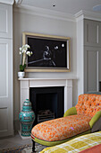Orchid on mantlepiece with artwork and upholstered chaise longue in bedroom of London home, England, UK