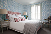Rosa Kopfteil und Wolldecke auf Doppelbett in blau gemustertem Schlafzimmer in London, England, UK