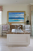 Large gilt-framed seascape above marble surround bath with shower fitting in Pewsey country house Wiltshire England UK