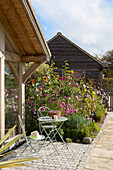 Blühende Pflanzen mit Tisch und Stuhl auf einer Terrasse in Surrey, England UK