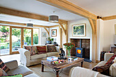 Lit woodburner and sofas with wooden coffee table in timber framed Surrey living room England UK