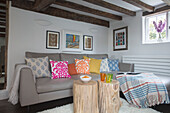 Wooden tree stumps and colourful cushions on grey leather sofa in beamed Surrey living room England UK