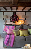 Lit candles and flowers on sideboard with gold and pink cushions on grey sofa in Surrey living room England UK