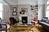 Cut flowers and books on glass topped coffee table with lit fire in Victorian family home in South West London UK