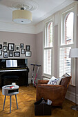 Brauner Ledersessel am Fenster mit Klavier und gerahmten Fotos in viktorianischem Familienhaus South West London UK