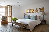 "Schnittblumen auf einer Bank am Fußende eines Doppelbetts mit dem Schriftzug DREAM"" in einem Haus in Arundel, West Sussex, England, Vereinigtes Königreich"""