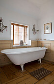 Venetian blinds at window above freestanding bath in wood panelled Arundel bathroom West Sussex England UK