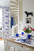 Blue glassware on dining table with spiral staircase in London townhouse UK