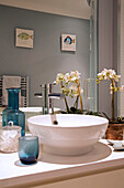 Orchid and washbasin with coloured glass and mirror reflection in London townhouse