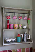 Red and pink cups with coffee flask on kitchen shelves in UK home