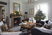 Lit candles and woodburner with Christmas tree in window of Surrey home England UK