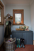 Hutständer und Korb mit Stiefeln unter Buntglasfenster in Haus in Surrey, England, UK