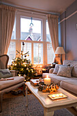 Beleuchtete Kerze auf einem Couchtisch mit Weihnachtsbaum am Fenster in einem Haus in London, England UK