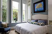 Floral bolster on double bed at windows in light blue bedroom of London townhouse UK