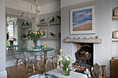 Glass dining table and collection of wooden birds with coastal landscape above fireplace in Sussex beach house England UK