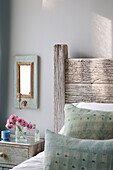 Wooden headboard and mirror with cut flowers at bedside in Sussex home England UK